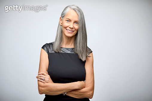 Portrait of smiling businesswoman with arms crossed. Confident mature professional is standing against white background. She is wearing business casuals. - gettyimageskorea