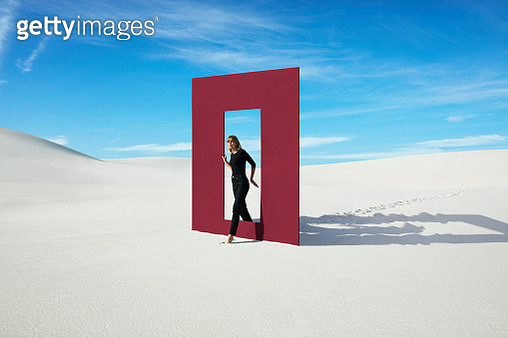 Young fashion model walking through red door frame at desert against sky - gettyimageskorea