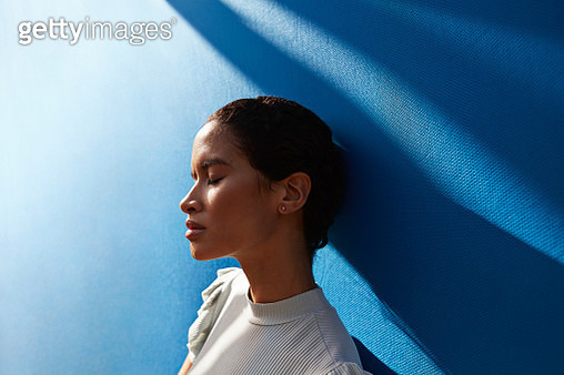 Beautiful woman standing against blue wall - gettyimageskorea