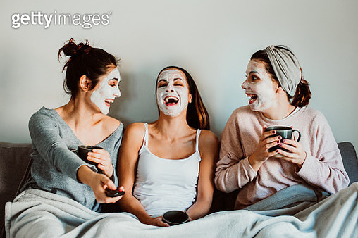 Cheerful Women With Facial Mask Sitting On Sofa At Home - gettyimageskorea