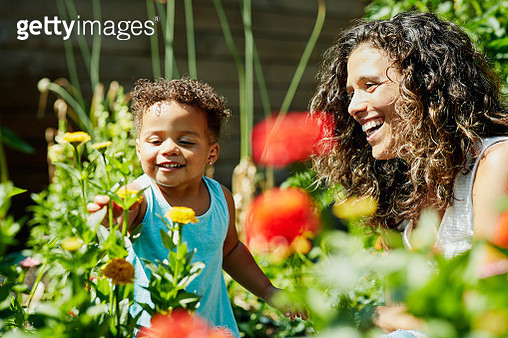 Smiling mother and toddler daughter enjoying flowers growing in backyard garden - gettyimageskorea